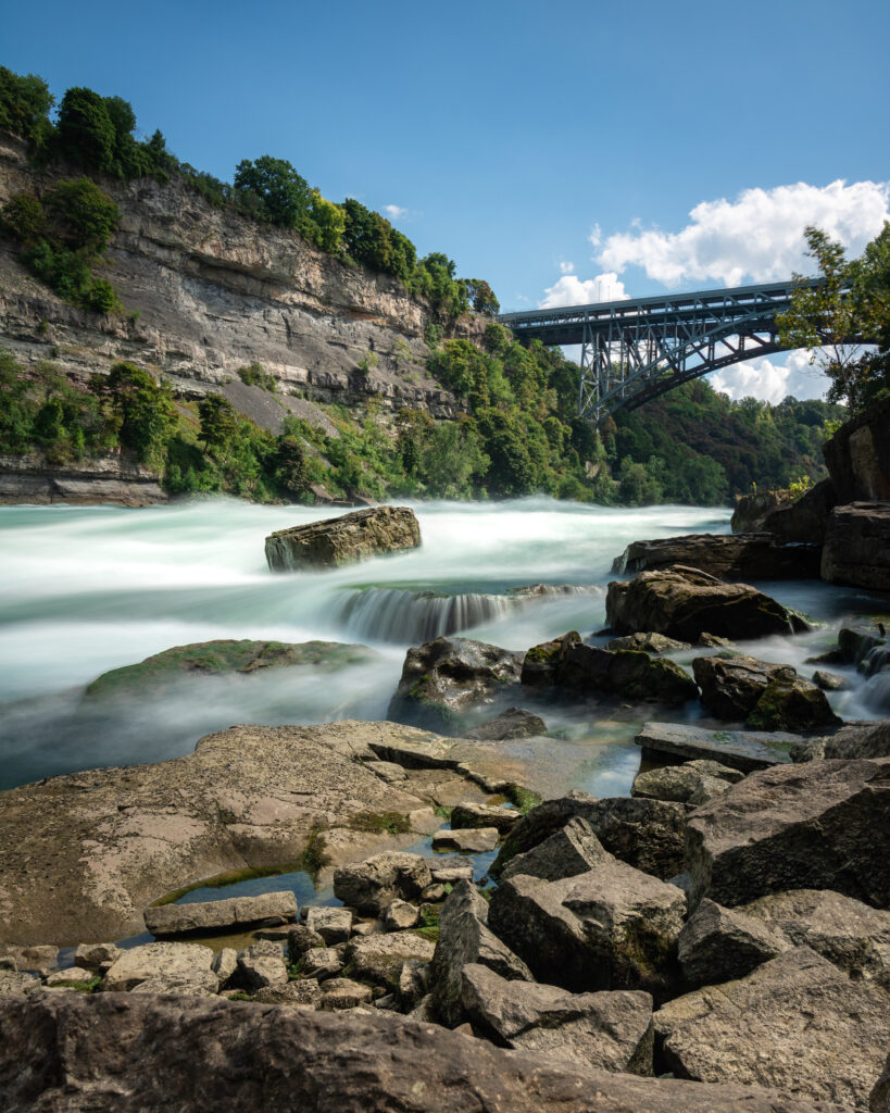 Metal bridge in the background over Niagara Falls with rushing water