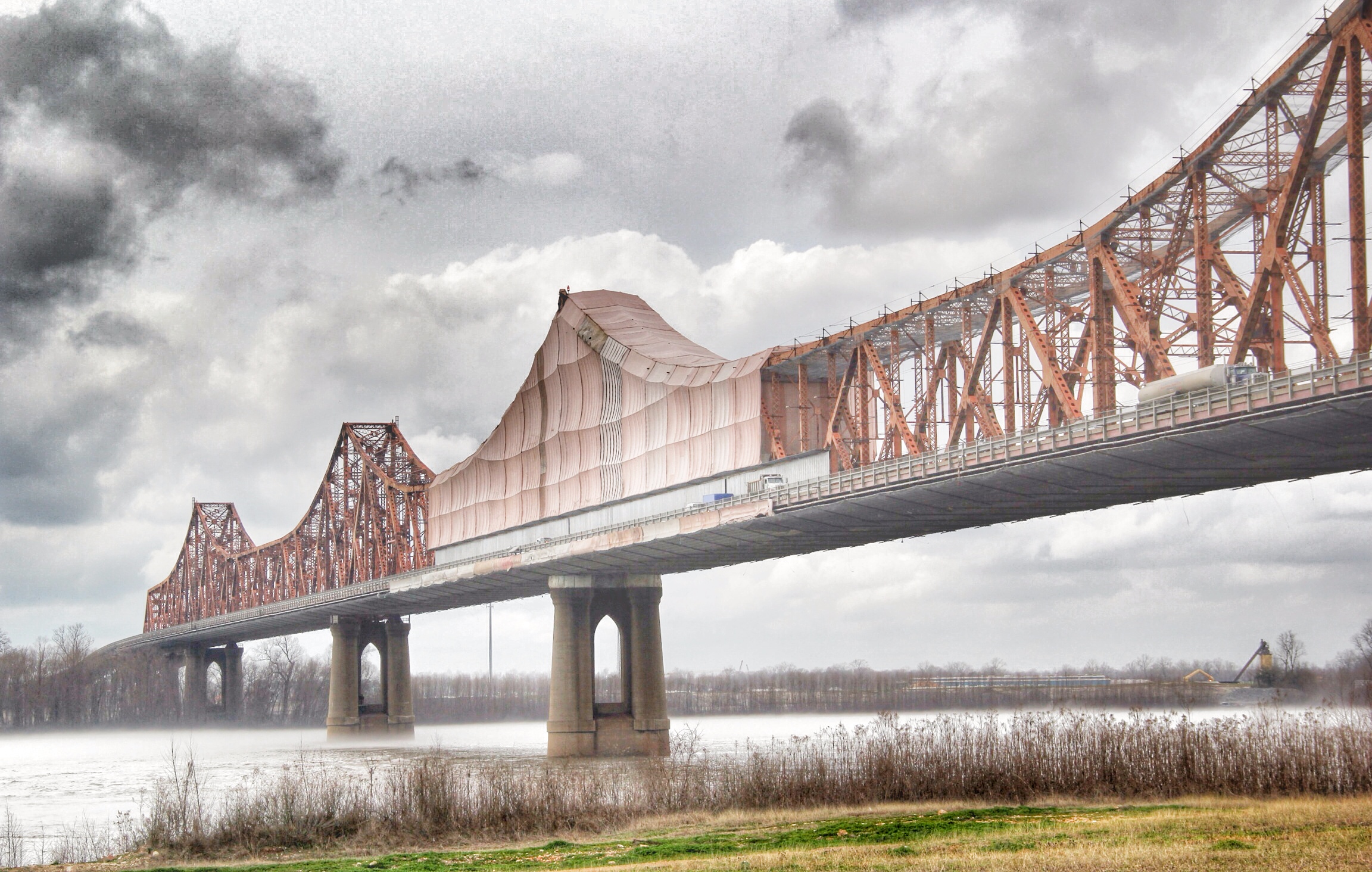 Red/orange Huey P Long bridge in Jefferson Parish with vehicles, trucks, and workers